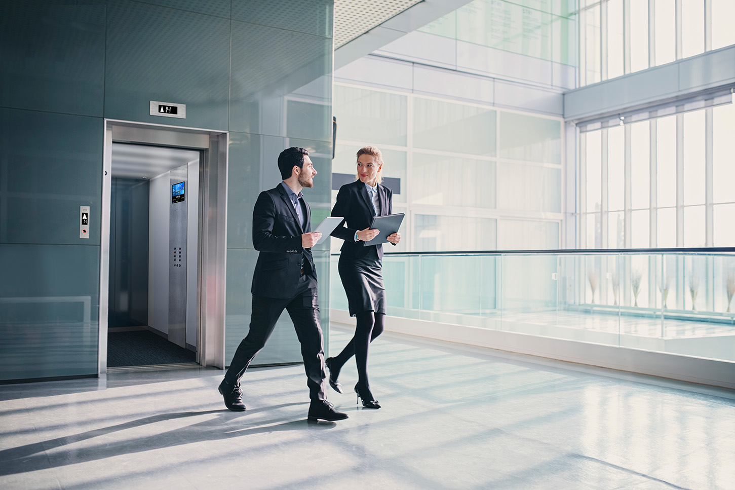 Two people walking out of an elevator with eView in-car display