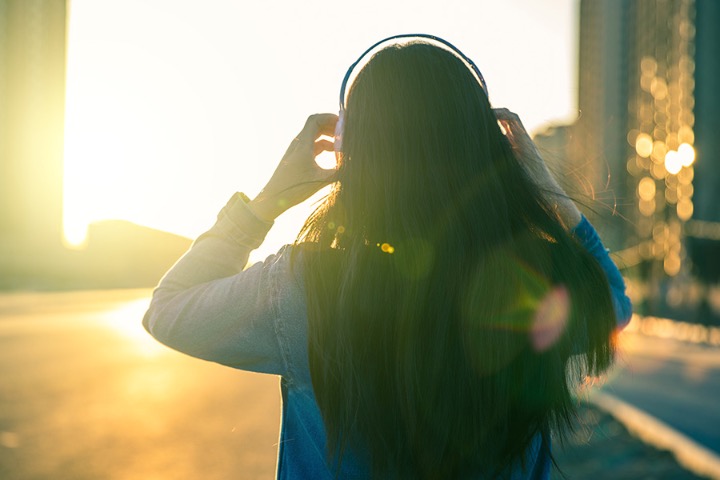young lady listening to headphones sunset