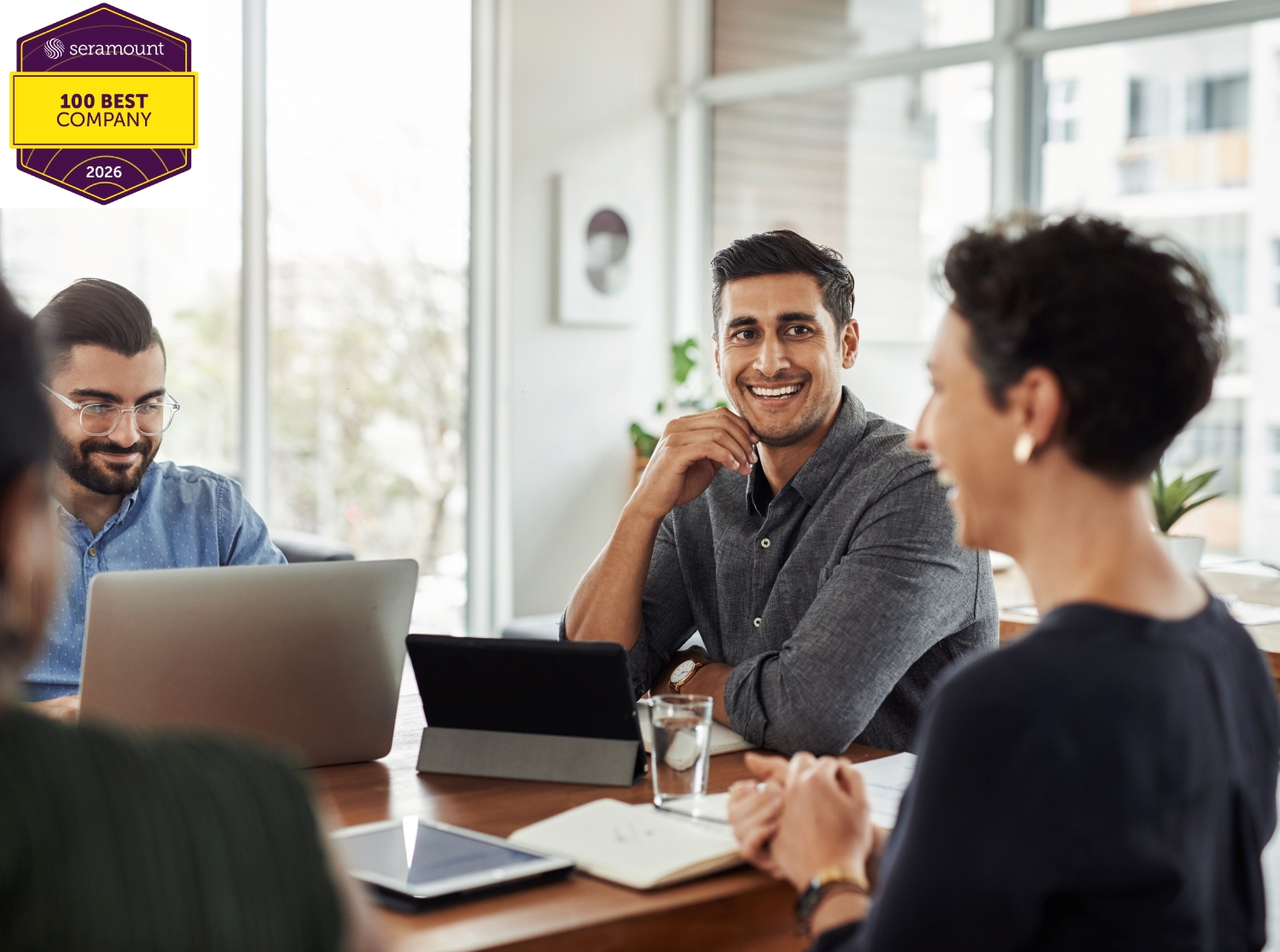Three Colleagues, two men and one woman having a friendly discussion in a bright, modern office meeting space.